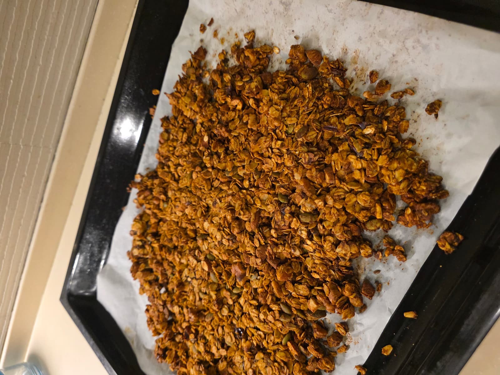 Freshly baked chocolate granola spread on a parchment-lined baking tray